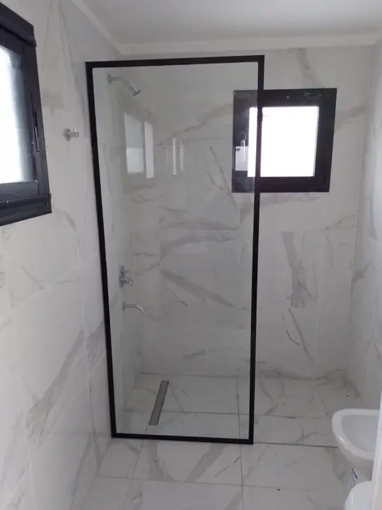 Fixed shower screen with a black profile in a white marble bathroom