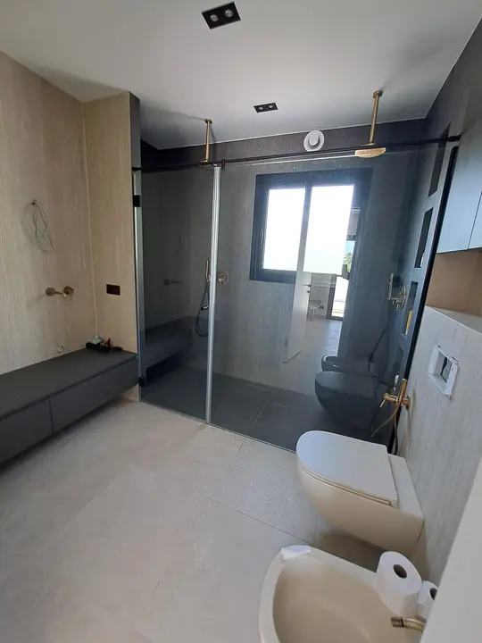 Walk-in shower screen in a grey bathroom with gold taps